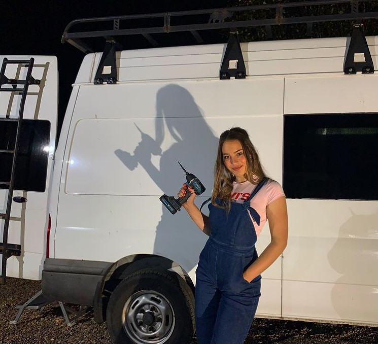 a woman called ame posing with a drill while standing outside by her large white van