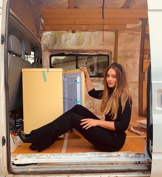 a woman named ame sitting inside of her van as she poses with a mini fridge