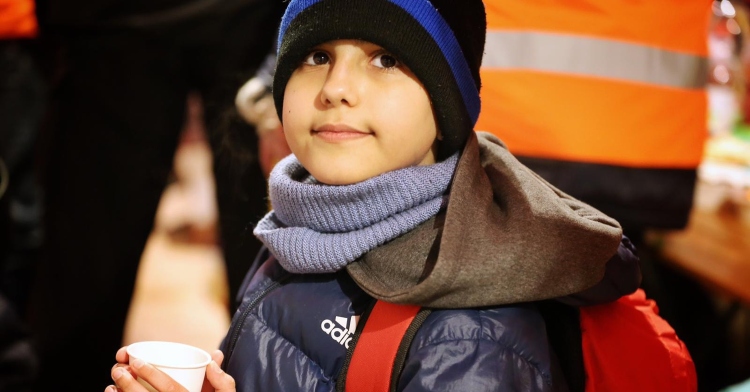 closeup of an 11-year-old boy named hassan who is holding a cup in his hand as he looks up and into the distance after making it to the slovakian border after fleeing ukraine