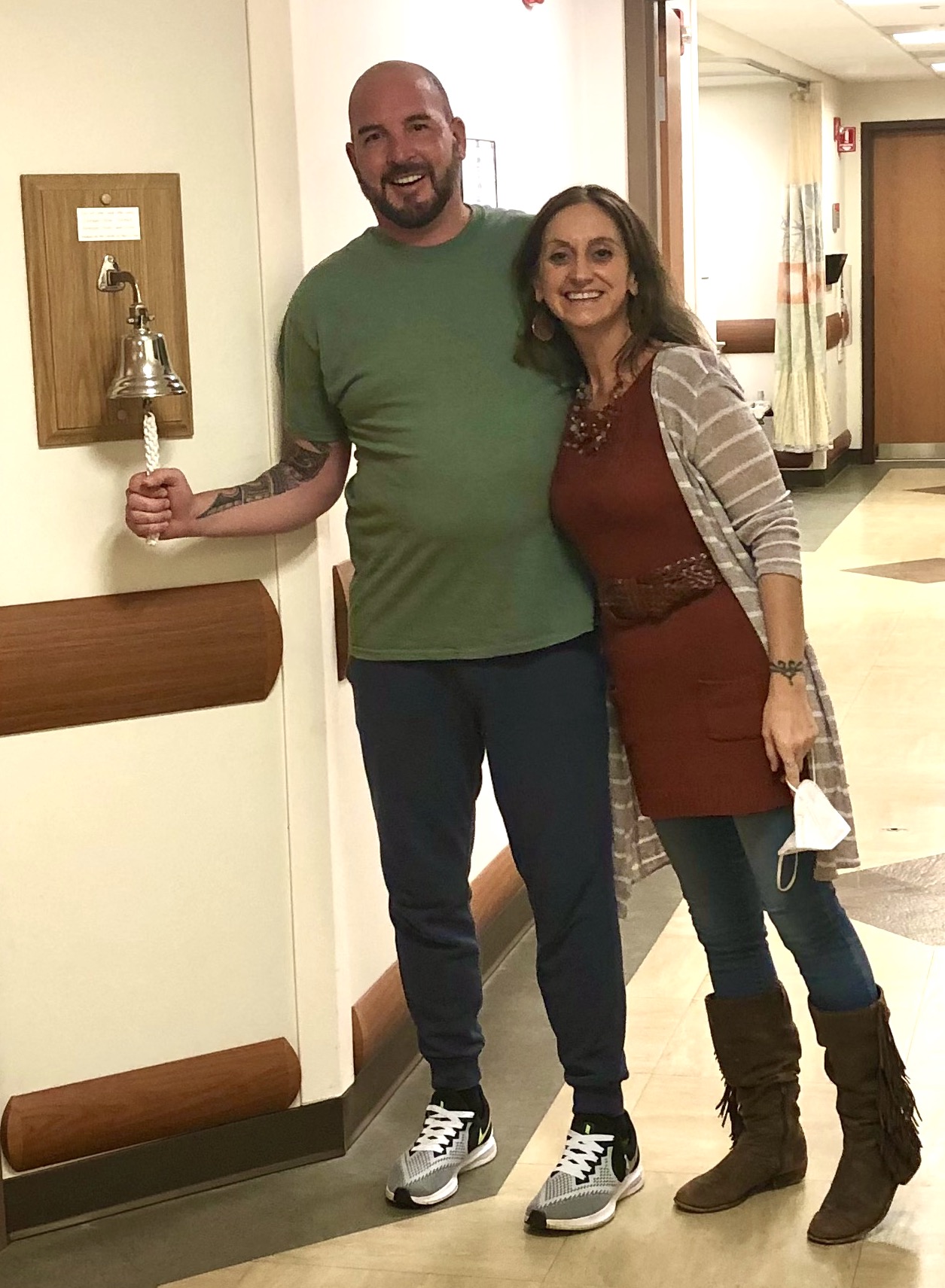 a man named adam miskow and a woman named jill ford posing and smiling as adam rings a bell in celebration of finishing his radiation treatment