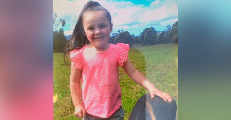 4-year-old shayla of tasmania smiling as she stands outside and rests one hand on a tire placed on the ground