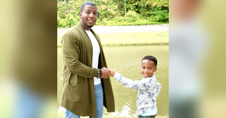 a man named justice smith smiling as he stands in front of a river and fist bumps his 5-year-old son named justus mateo