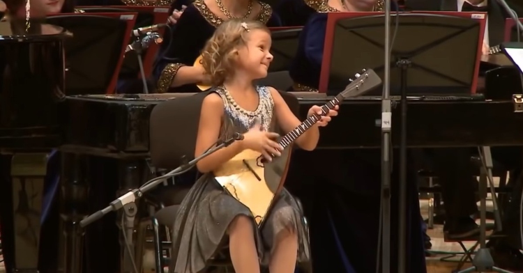 7-year-old anastasiia tiurina smiling as she plays “valenki” on her balalaika with the national academic orchestra of russian folk