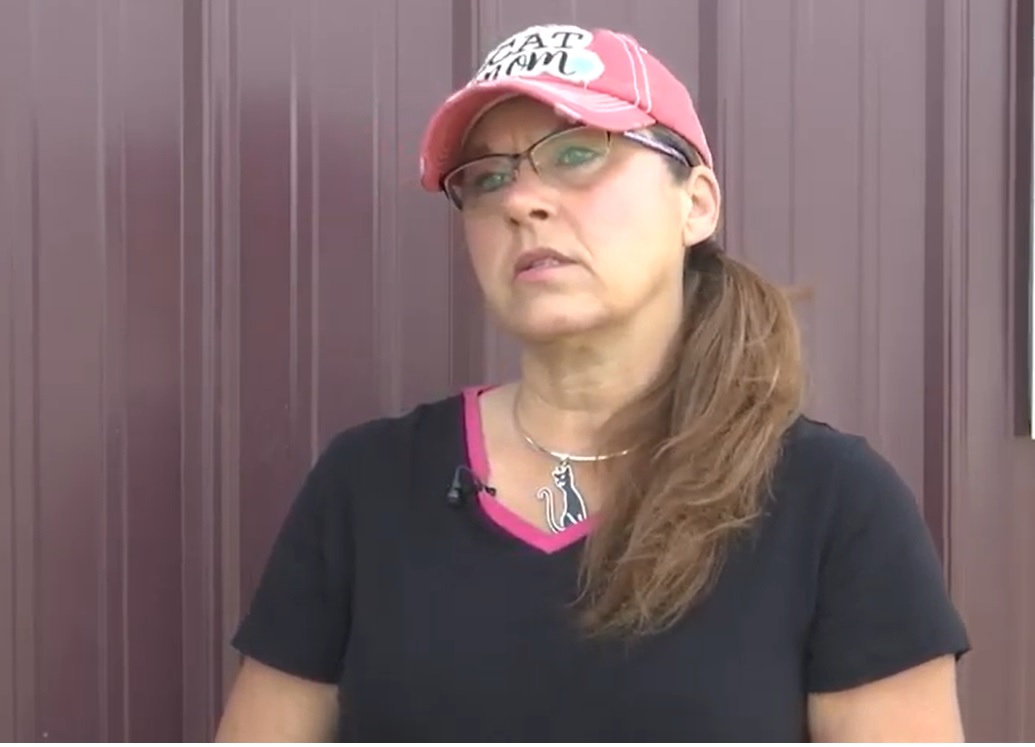 jackie mihal talking outside in front of a building. she is wearing a hat that says "cat mom" and a necklace with a back cat on it.