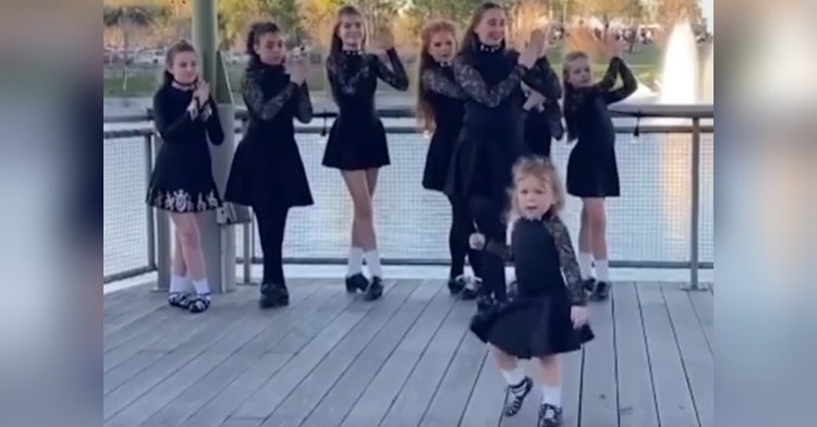 three-year-old zoe surrell performing an irish step dance while older dancers standing behind her.