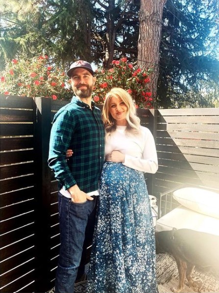 a man named bryan hill smiling and posing outside with his wife, julia horner, who is pregnant