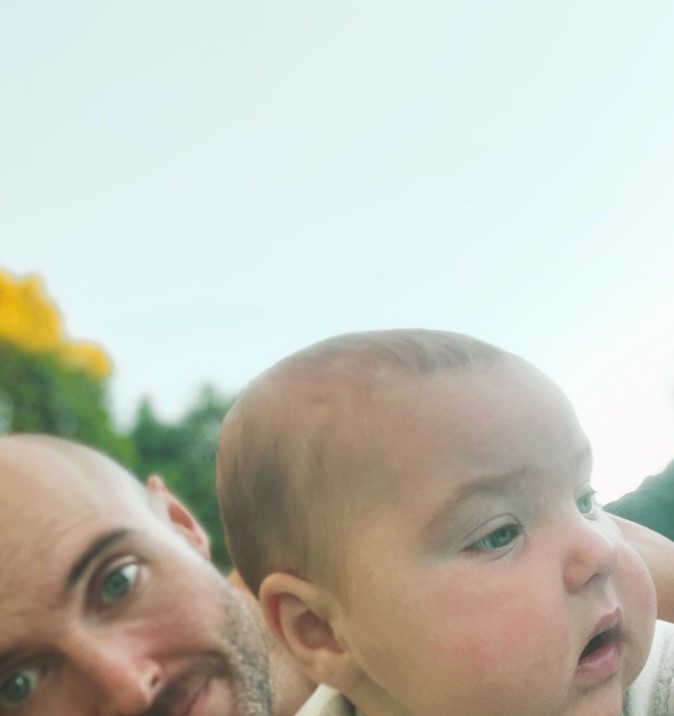 closeup of a man named bryan hill and his baby boy, forrest, laying on the ground outside 