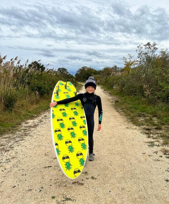 an 11-year-old boy named carter doorley smiling and posing with a yellow surfboard with pineapples on it