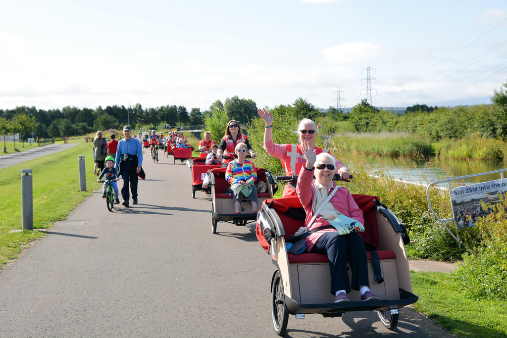 a line of people on trishaws with two smiling women who are waving leading the group