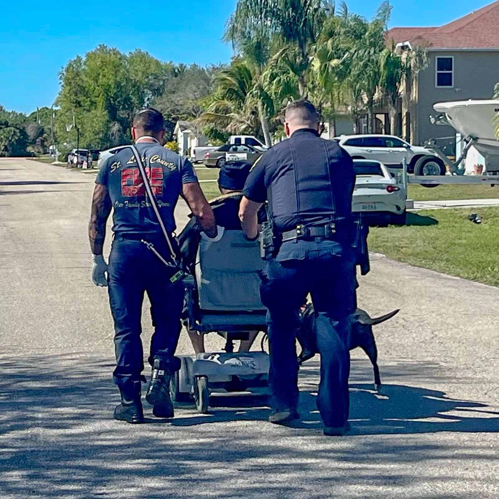a police officer and a fireman pushing an 81 year old man named harry smith down the road in his broken electric wheelchair so he can go home