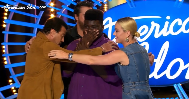 “american idol” judges katy perry, luke bryan, and lionel richie gathering for a group hug with 18-year-old contestant douglas mills who just auditioned with “strange fruit” by billie holiday