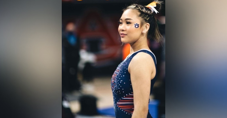 18 year old sunisa lee looking out at the crowd as she wears her auburn university gymnastics uniform and has the auburn university symbol painted on the side of her face