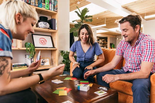 three adults sitting in a living room around a coffee table as they play a card game together