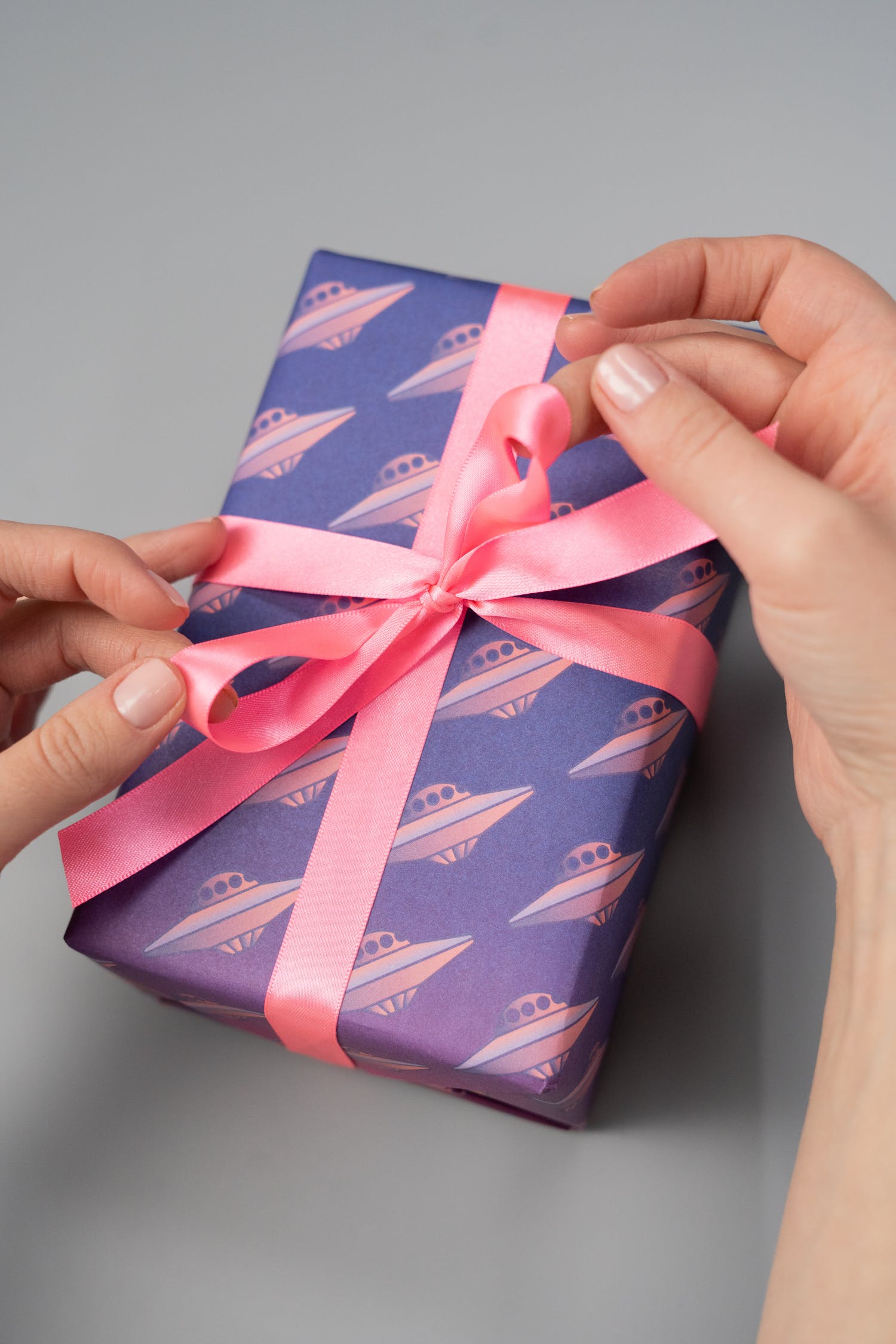 closeup of woman tying a bow on a wrapped gift that's purple and has pink ufos on it