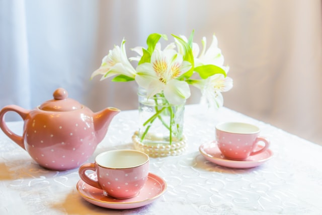a child's tea set with a polka-dot tea tea pot, cups, and saucers next to a small container of white flowers