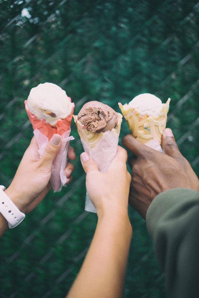 closeup of three different kinds of ice cream cones with three different people holding them