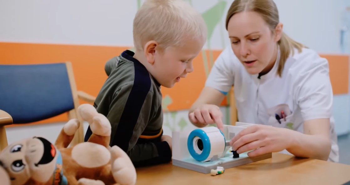 a little boy and a medical professional playing with a miniature lego mri scanner 