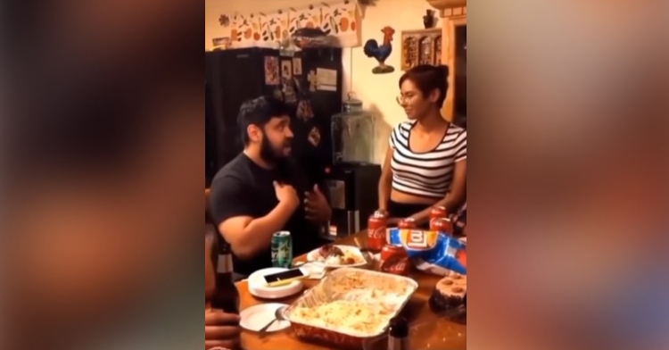 a man sitting at a dining table using sign language to sing “a thousand years” by christina perri to his girlfriend who is standing next to him