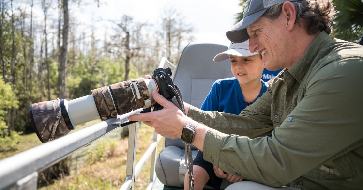 national geographic wildlife photographer carlton ward showing an 8-year-old boy named oban how to use his camera as they explore florida's audubon corkscrew swamp sanctuary