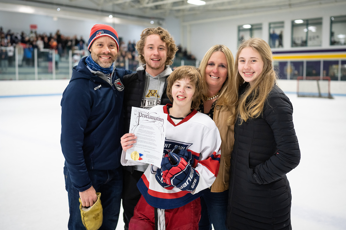 13-year-old owen nei smiling with his dad, chris nei, along with his mom, older brother, and sister as he holds a proclamation from the mayor stating february 11th is owen nei day in st. paul 