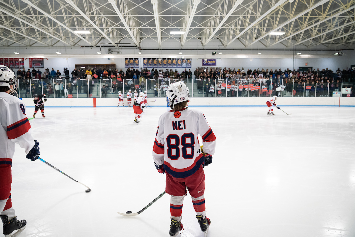 view of the back of 13-year-old owen nei as he stands on the ice before a st. paul capitals hockey game and looks out into the crowd