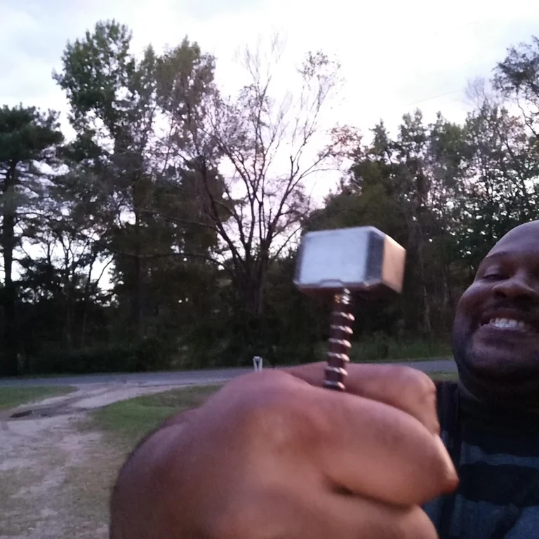 a man taking a selfie while holding a miniature mjolnir close to the camera