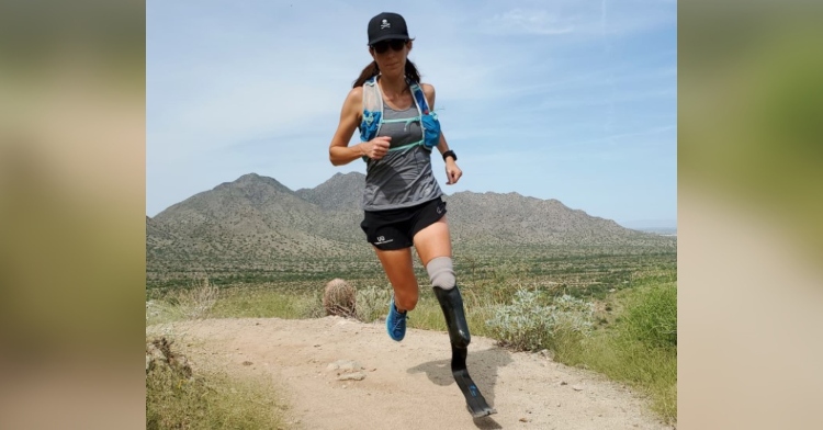 jacky hunt-broersma running outside with large mountains in the distance. she has a prosthetic leg and is wearing a baseball cap and sunglasses.