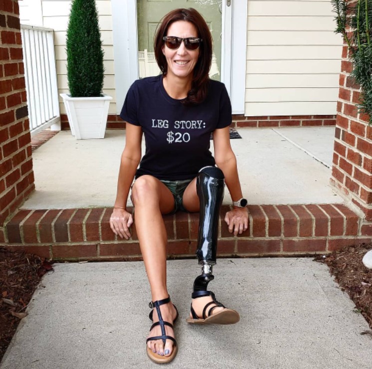 a woman named jacky hunt-broersma. she is an amputee with a prosthetic leg. she smiles as she sits on a front porch. she's wearing sunglasses and a shirt that says 