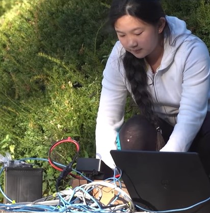anna du squatting down outside to work with equipment she's put together for her remote-operated vehicle (rov) made to detect plastics on the ocean floor.