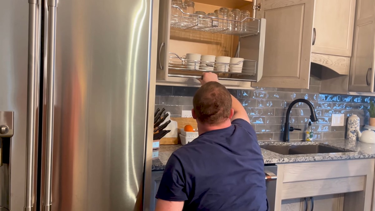 retired u.s. army sergeant christopher kurtz pulling down a tray from a kitchen cabinet in his new smart home that holds his glassware 