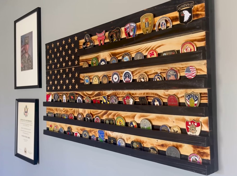wall in the home of retired u.s. army sergeant christopher kurtz. hanging on the wall is a wooden american flag with shelves holding military pins. next to that is a framed photo of christopher during his time in the military and a framed certificate 