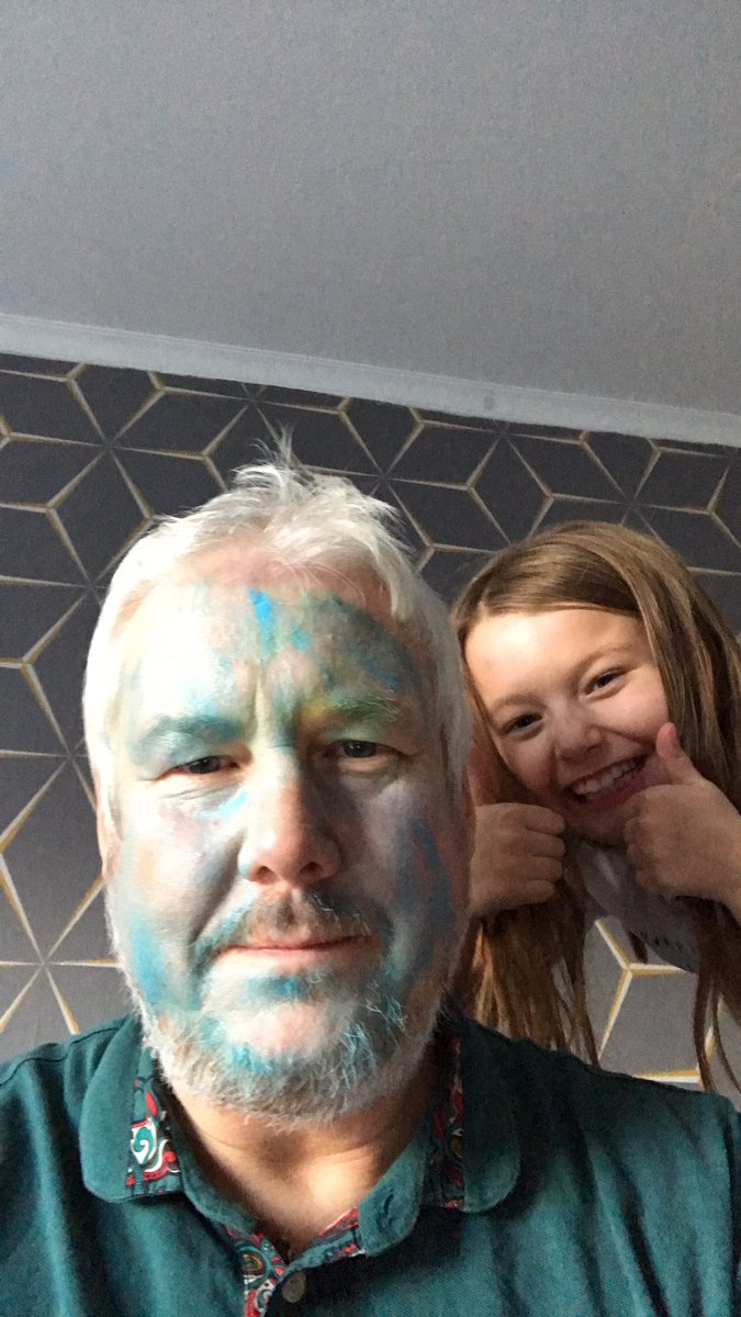 girl doing a thumbs-up while her dad's face is covered in blue. 