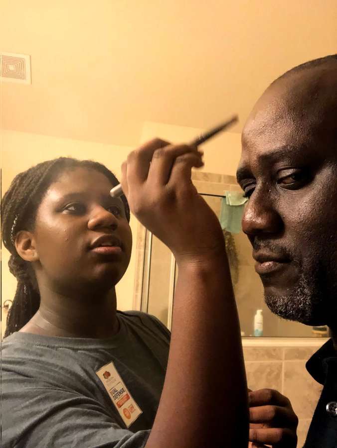 girl doing her dad's makeup while he stares at the camera.