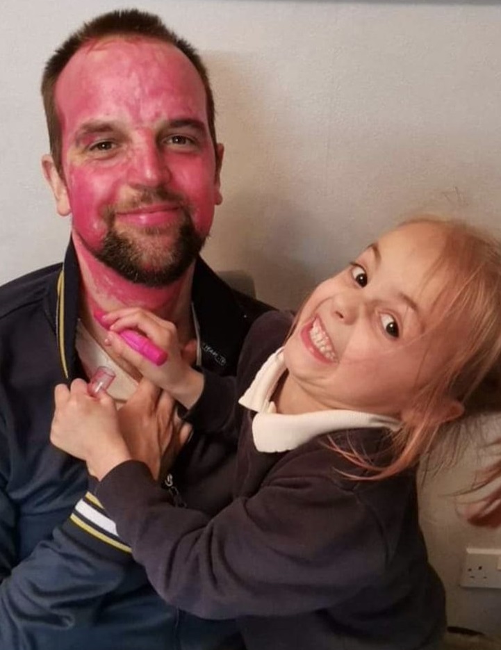 little girl holding a pink lipstick and covering his dad's face with it.