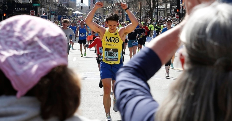 20-year-old henry richard finishing the crossing line of his first boston marathon. he has both fists in the air as he emotionally looks down at the ground.