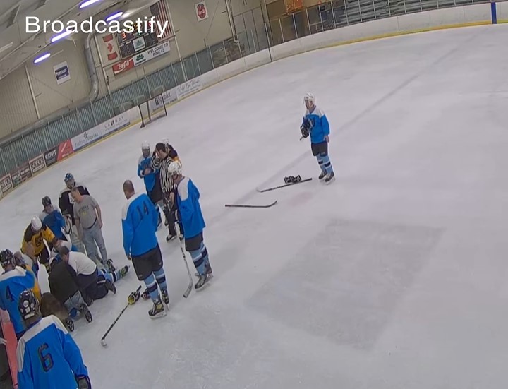 security camera footage of various hockey players standing around a sylvania tamoshanter hockey player, bruce tronolone, who is laying on the ice as he suffers from cardiac arrest.