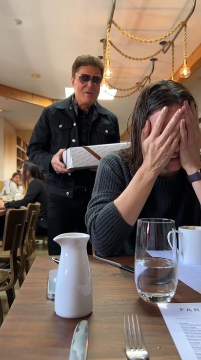 donny osmond surprising jennifer garner for her 50th birthday. garner is sitting at a table in a restaurant. she's covering her face with her hands as she smiles. osmond is standing behind her. he's holding a box containing a cake and is singing.