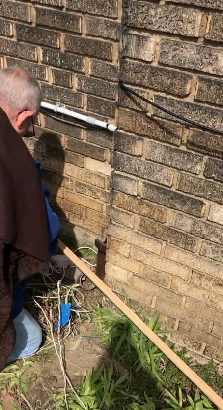 a man, who is on his knees, using a device that was made to help them rescue a kitten. the kitten fell into a drain pipe that is 8 feet deep.
