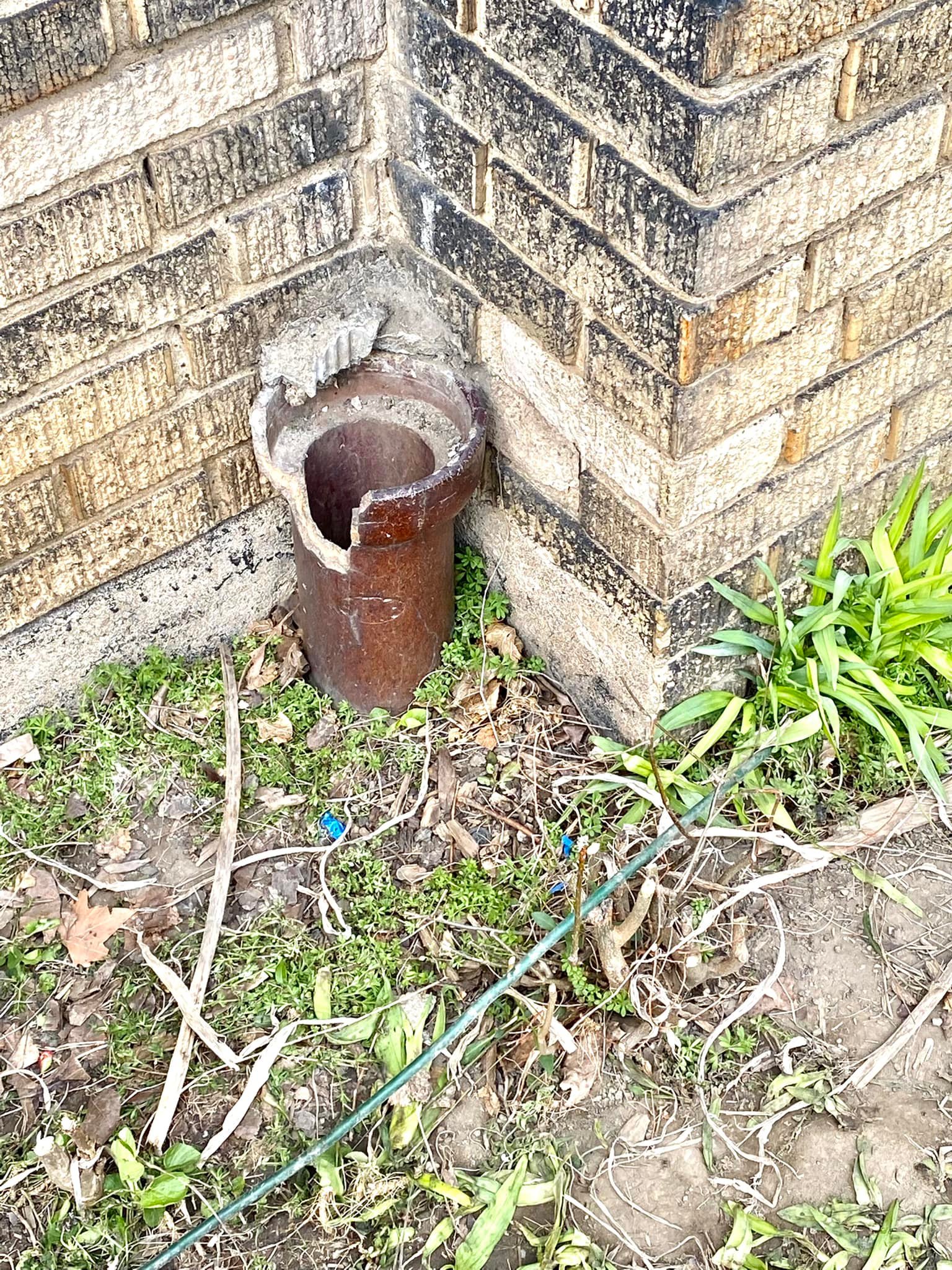 an uncovered drain pipe in the corner of a house made of brick. the house is in cleveland, ohio. inside is a stuck kitten.