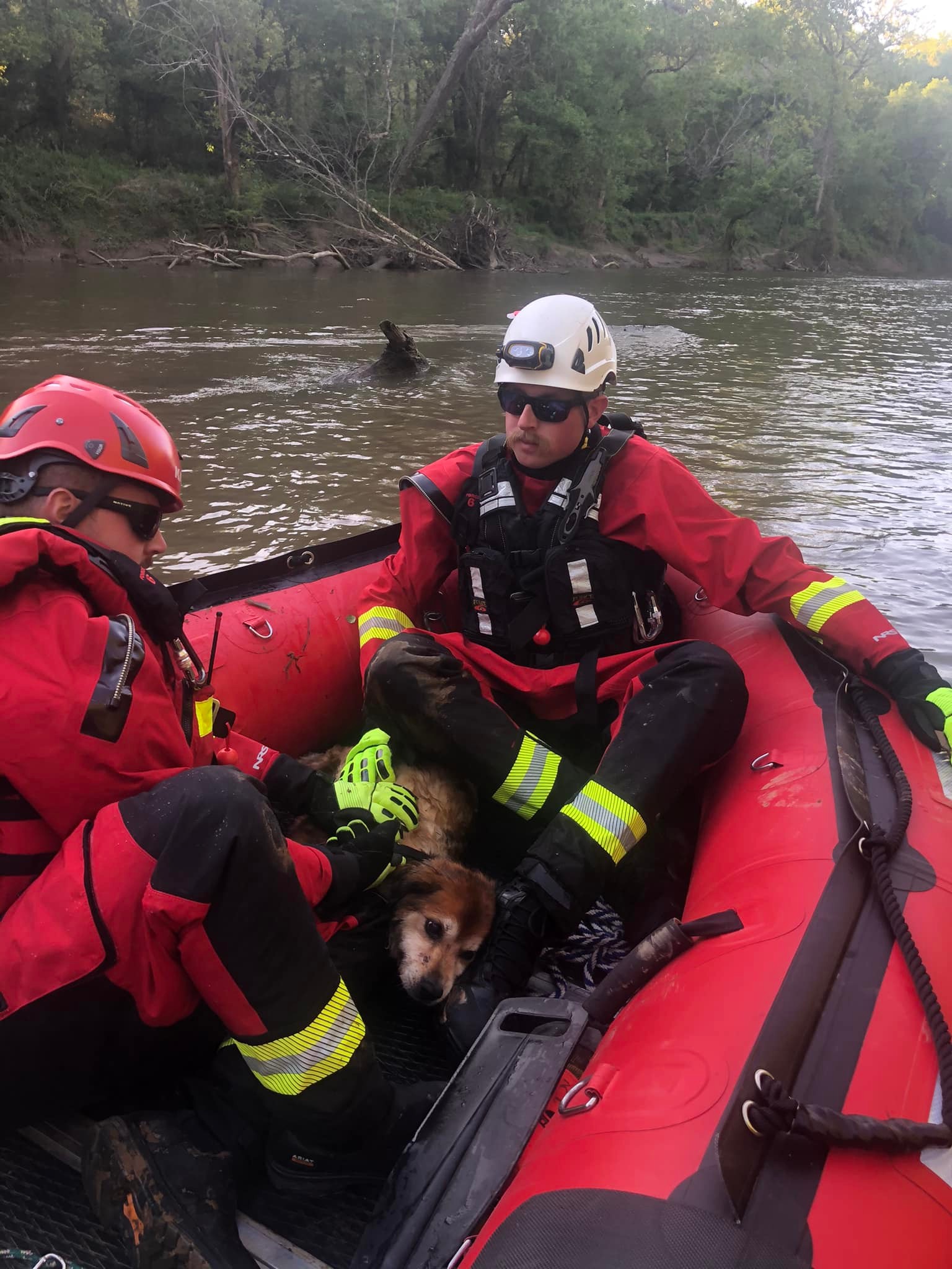 two firefighters from the knightdale fire department sitting in a boat on nesue river. one of them is petting a dog they rescued who is laying on the floor of the boat.