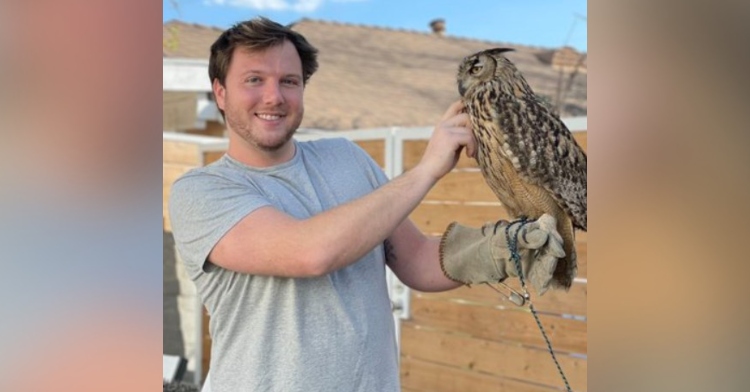 closeup of scott thiede. he’s smiling as he holds an owl with one hand and pets it with the other. he’s wearing a glove on the hand he’s using to hold the owl.