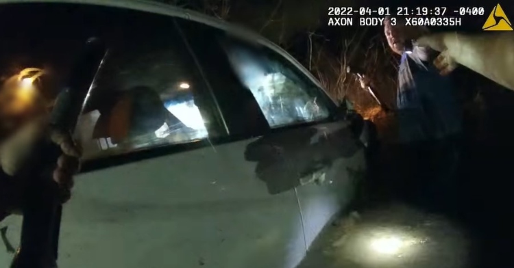 screenshot from police body cam footage from the arundel county police department. there is a car that is half-submerged in a pond in a park. a second police office can be seen toward the front of the car.