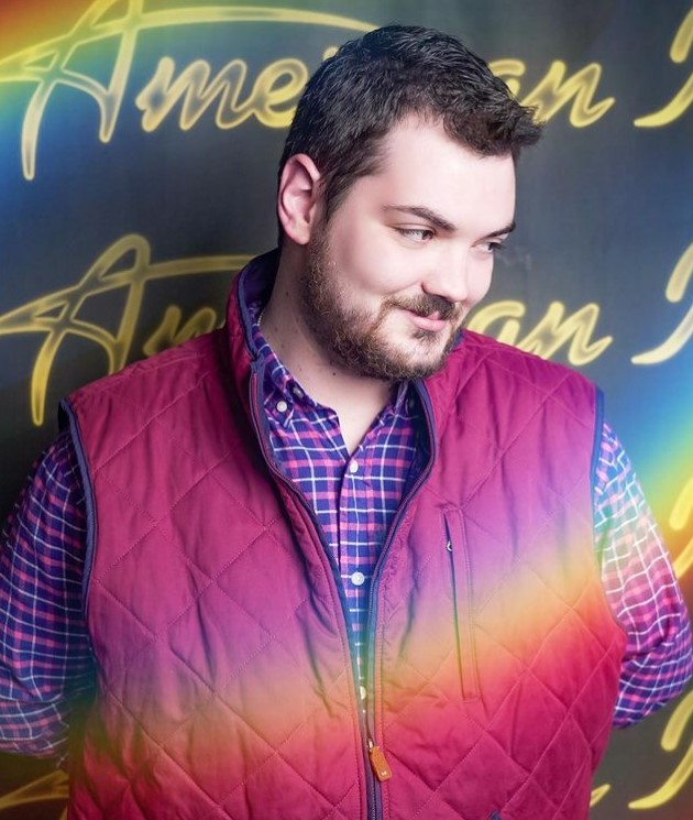 "american idol" contestant sam finelli smiling and looking away as he poses in front of an "american idol" backdrop.