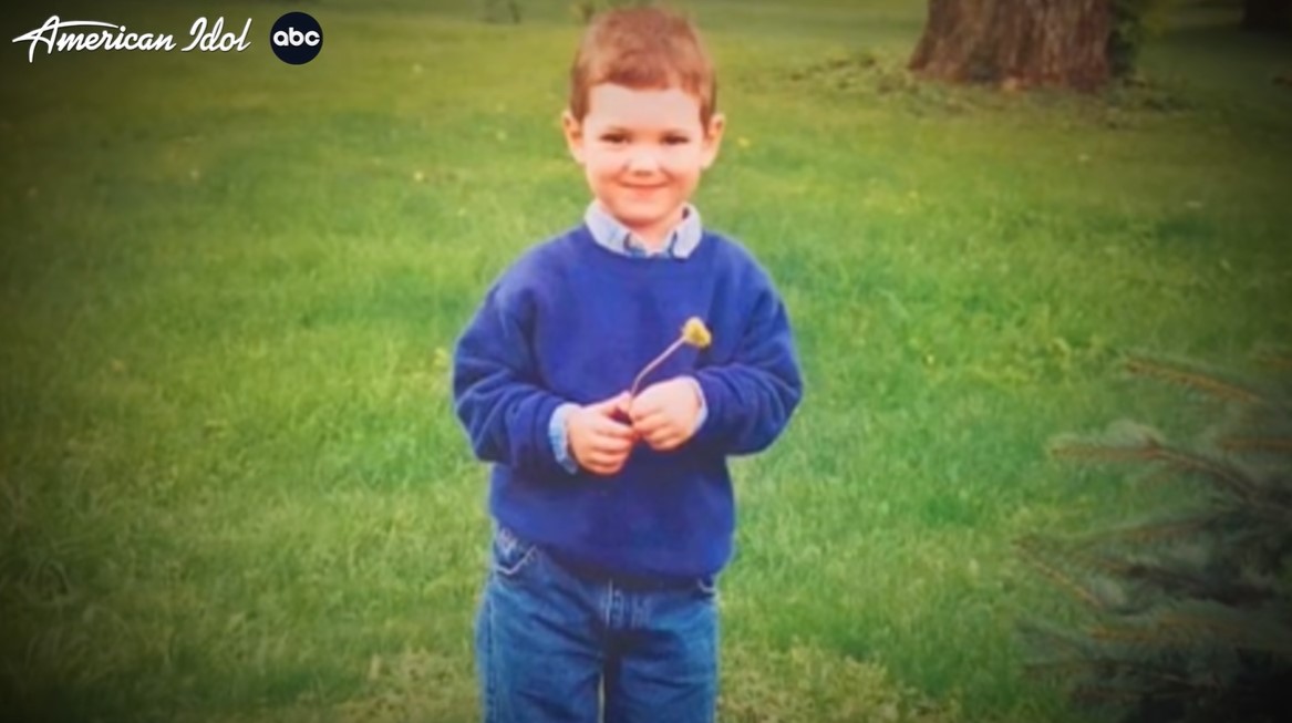 "american idol" contestant sam finelli as a child smiling and holding a flower while standing outside