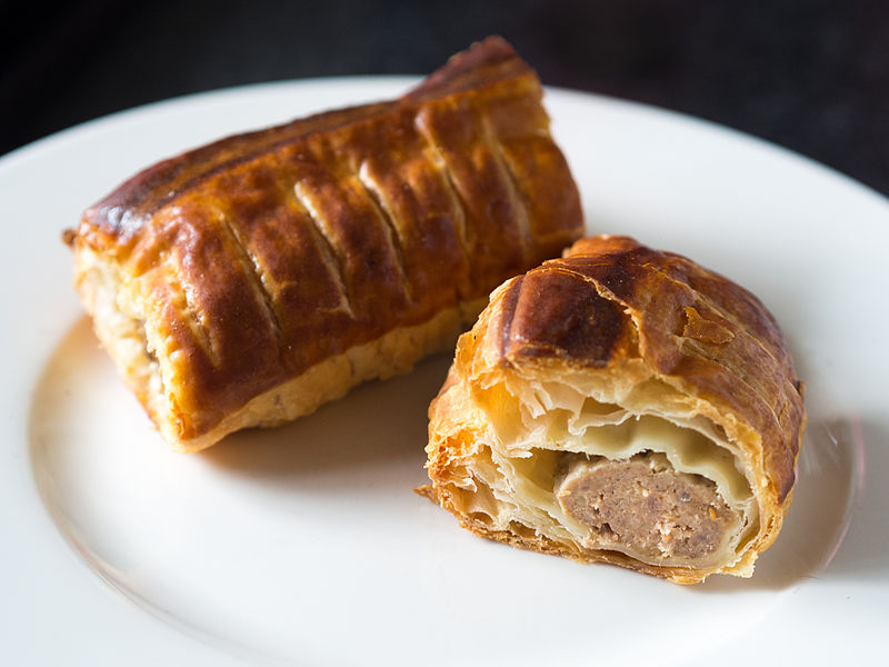 closeup of two sausage rolls placed on a white plate. one sausage roll is cut so that the inside can be seen.