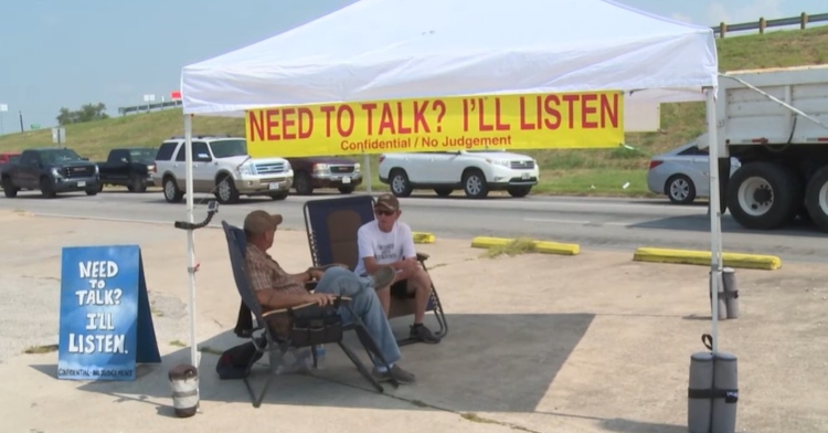 a tent set up by will norman in azle, texas. the tent has a sign that reads "need to talk? I'll listen. confidential/no judgement." underneath the tent are two chairs, one where will is sitting an another where a different man is sitting.