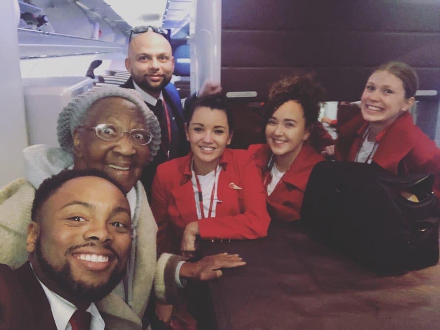 88-year-old violet smiling wide with virgin airlines crew while on a plane.