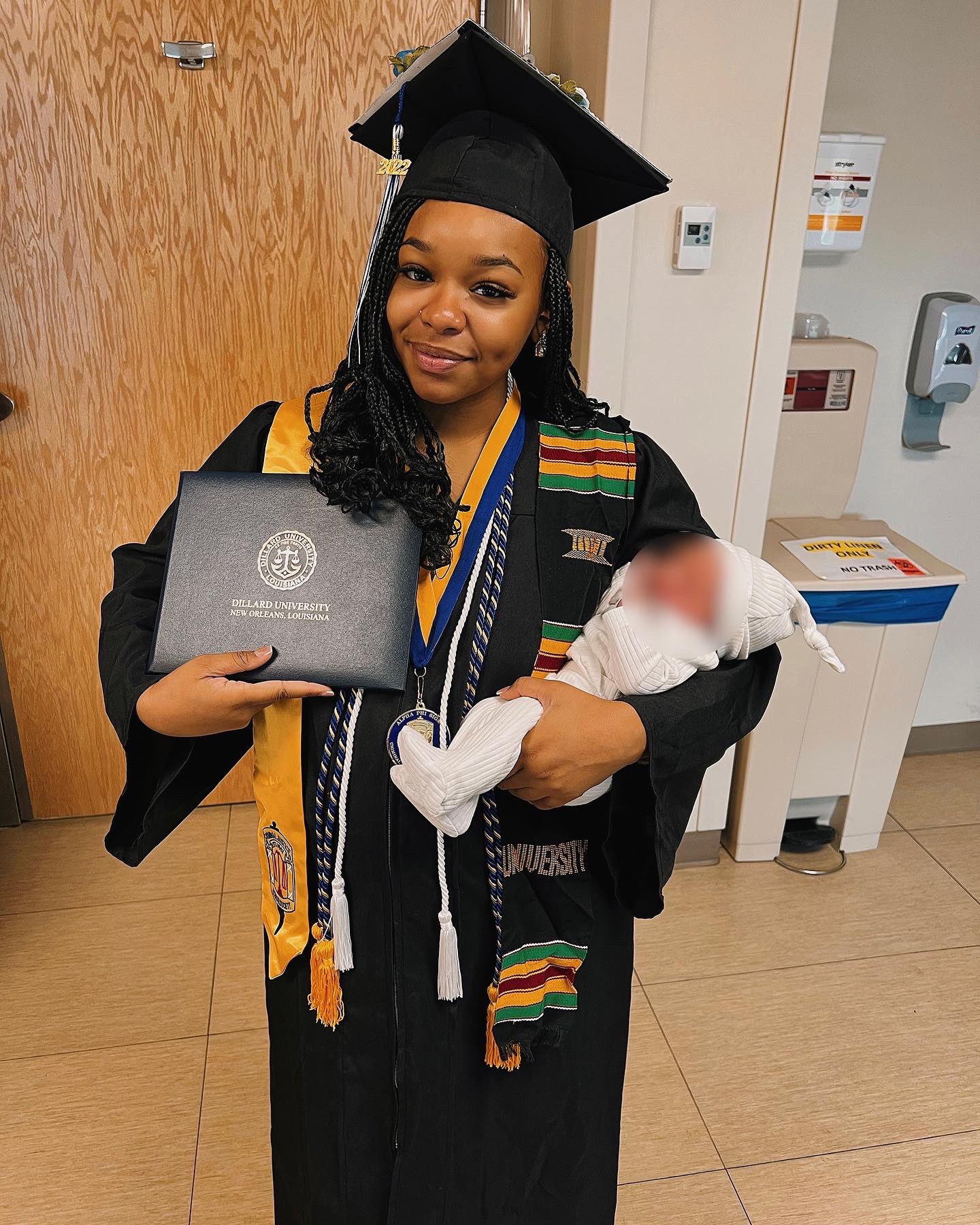 Jada Sayles holding her degree on one hand and her son on the other