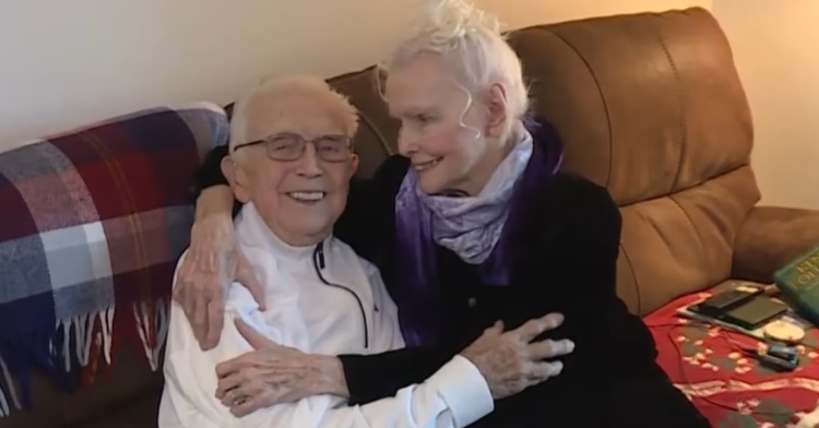 kenneth and elizabeth gage smiling as they sit together on a couch with their arms around each other. he's looking forward while she's looking at him.