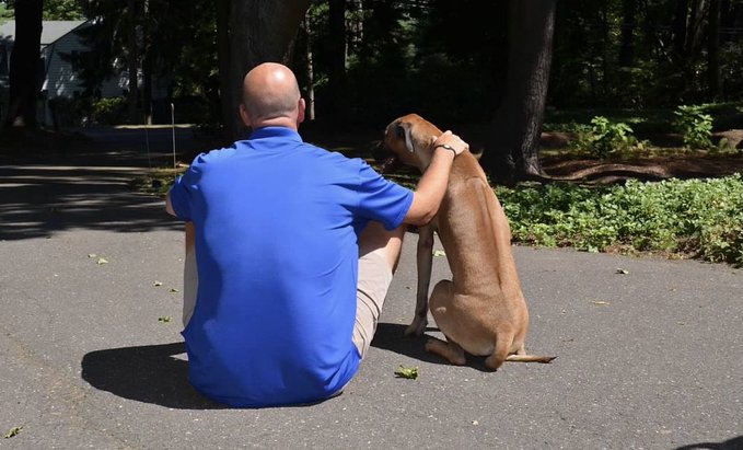 view from behind of scott van pelt sitting with his dog, otis, on a road outside. scott has his arm around otis.
